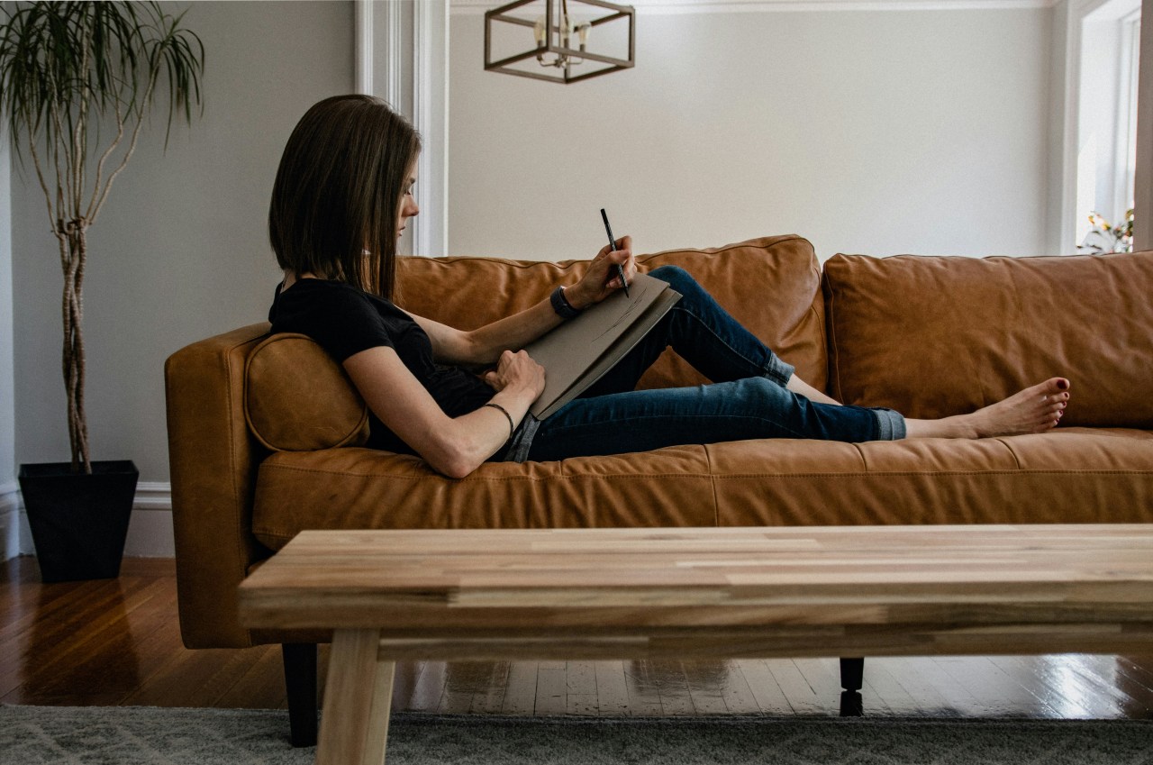 Selbstständige Frau arbeitet entspannt auf dem Sofa mit Notizbuch — Human Design im Business ermöglicht flexible und energiegerechte Arbeitsweise